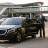 Business sedan airport transfer Melbourne with a professional chauffeur beside an executive sedan.